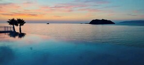 A tranquil infinity pool with a sunset view, palm trees, and a distant island. - Lesvos Greek Island, Birds Bay (Lesvos)