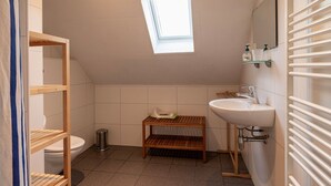 Ett litet badrum med ett takfönster, en hylla i trä, ett handfat och en toalett.