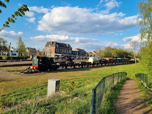 Ein Bahnhof mit einem stehenden Zug, Gleisen und einem Gebäude im Hintergrund.