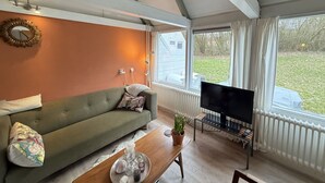 Un salon comprenant un canapé, une table basse, un téléviseur et une fenêtre donnant sur l’extérieur.