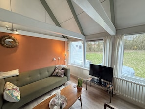 Ein Wohnzimmer mit einer Couch, einem Couchtisch, einem Fernseher und einem Fenster mit Blick nach draußen.