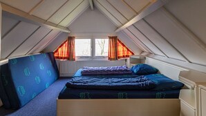 Una camera in stile dormitorio con soffitto spiovente, una finestra con tende, un letto con lenzuola blu e un termosifone.