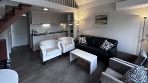 Un espace de vie moderne comprenant un escalier, une cuisine, un canapé noir, des fauteuils blancs et une table basse.