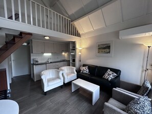 A modern living space with a staircase, a kitchen, a black sofa, white armchairs, and a coffee table. - Bungalowpark Simpelveld - Delta 128 by Interhome (Simpelveld)