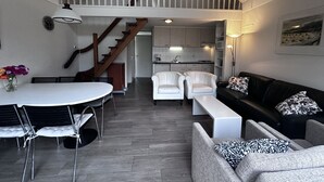Un vaste espace de vie comprenant une table à manger, des chaises blanches, un canapé noir et un escalier menant à un niveau supérieur.