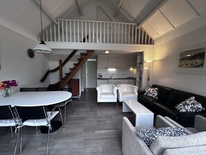 A spacious living area with a dining table, white chairs, a black sofa, and a staircase leading to an upper level. - Bungalowpark Simpelveld - Delta 128 by Interhome (Simpelveld)