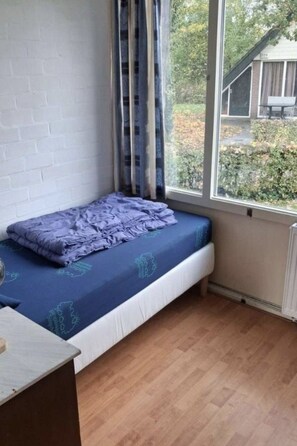 Ein kleines Zimmer mit einem Einzelbett, einem Fenster mit Vorhängen, einer Backsteinwand und einem Heizkörper.