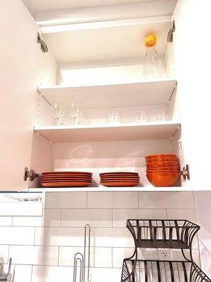Eine Küche mit weißen Schränken, einer hängenden orangefarbenen Schüssel und einem schwarzen Metallregal.