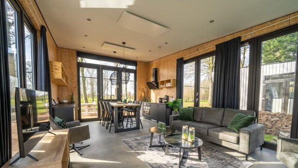 A modern living room with a sofa, coffee table, and dining area. - Vakantiepark Aan de Maas - Weide Lande 4 personen by Interhome (Kerkdriel)