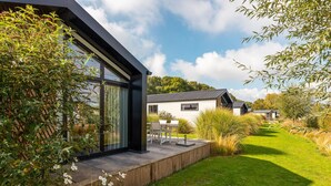 Una casa moderna con fachada de vidrio, terraza de madera y césped cuidado.