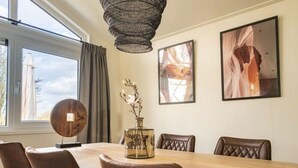 Uma sala de jantar com mesa de madeira, cadeiras de couro, luminária pendente e quadros nas paredes.