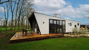 A modern house with a wooden deck, large glass doors, and a sloped roof. - Vakantiepark Aan de Maas - Weide Lande 6 personen by Interhome (Kerkdriel)