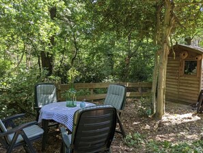 Eine rustikale Holzhütte mit Tisch und Stühlen vor der Tür, umgeben von dichtem Grün.