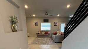 A spacious living area with a herringbone-patterned floor, a ceiling fan, and a sofa set.