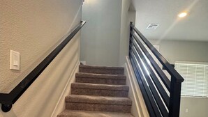A carpeted staircase with black handrails, a light switch, and a window at the top.