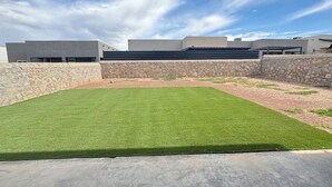 A courtyard with a green lawn, stone walls, and modern buildings in the background.