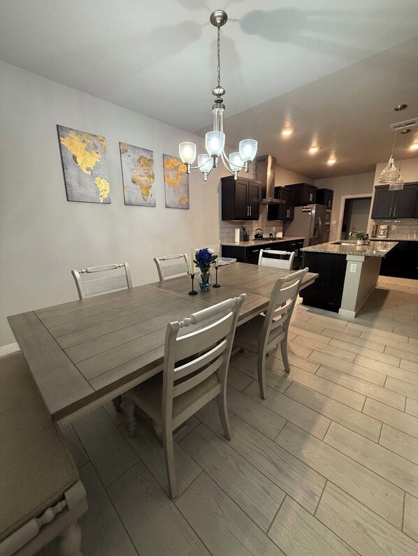 A modern kitchen with dark cabinets, a central island, and a dining area with a wooden table and chairs.