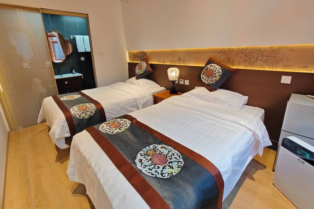 Una habitación de hotel con dos camas, un espejo, una mesita de noche con lámpara, un calefactor y un armario.