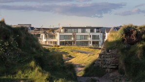 A modern building with a flat roof, large windows, and a paved driveway leading to the entrance. - Perrantide (Bude)