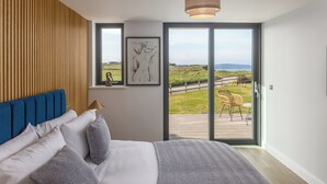 A bedroom with a large bed, a wooden slat wall, a ceiling light, and a view of a deck and landscape. - Perrantide (Bude)