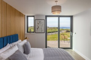 Une chambre avec un grand lit, un mur recouvert de lambris en bois, un luminaire au plafond et une vue sur une terrasse et le paysage environnant.