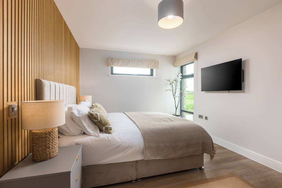 A modern bedroom with a bed, bedside lamp, TV, and a window with curtains.