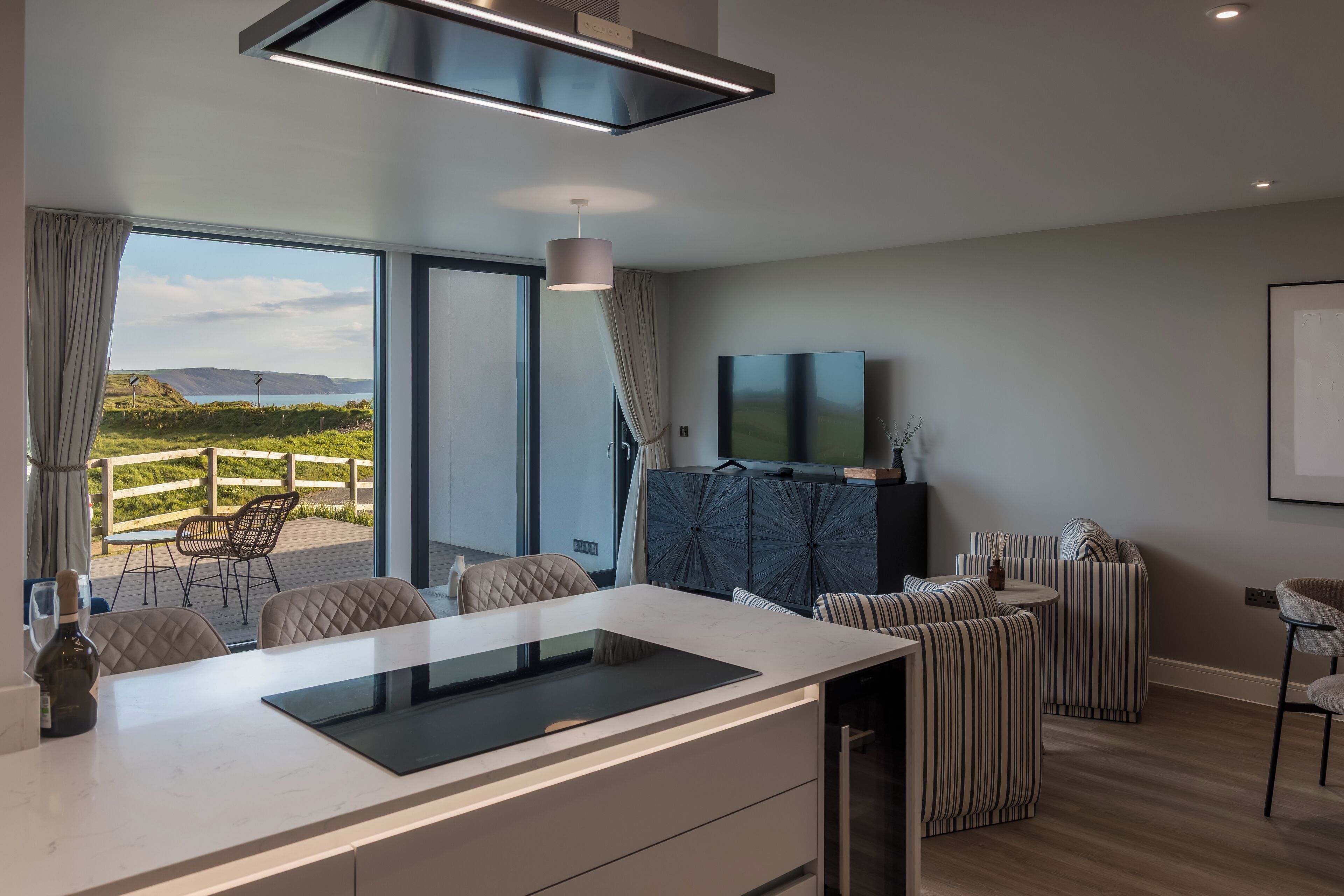 A modern kitchen with a large island, a dining area with chairs, a TV, and a view of the outdoors.