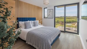 A bedroom with a large bed, a wooden slat wall, a view of the outdoors, and a balcony with chairs. - Perrantide (Bude)