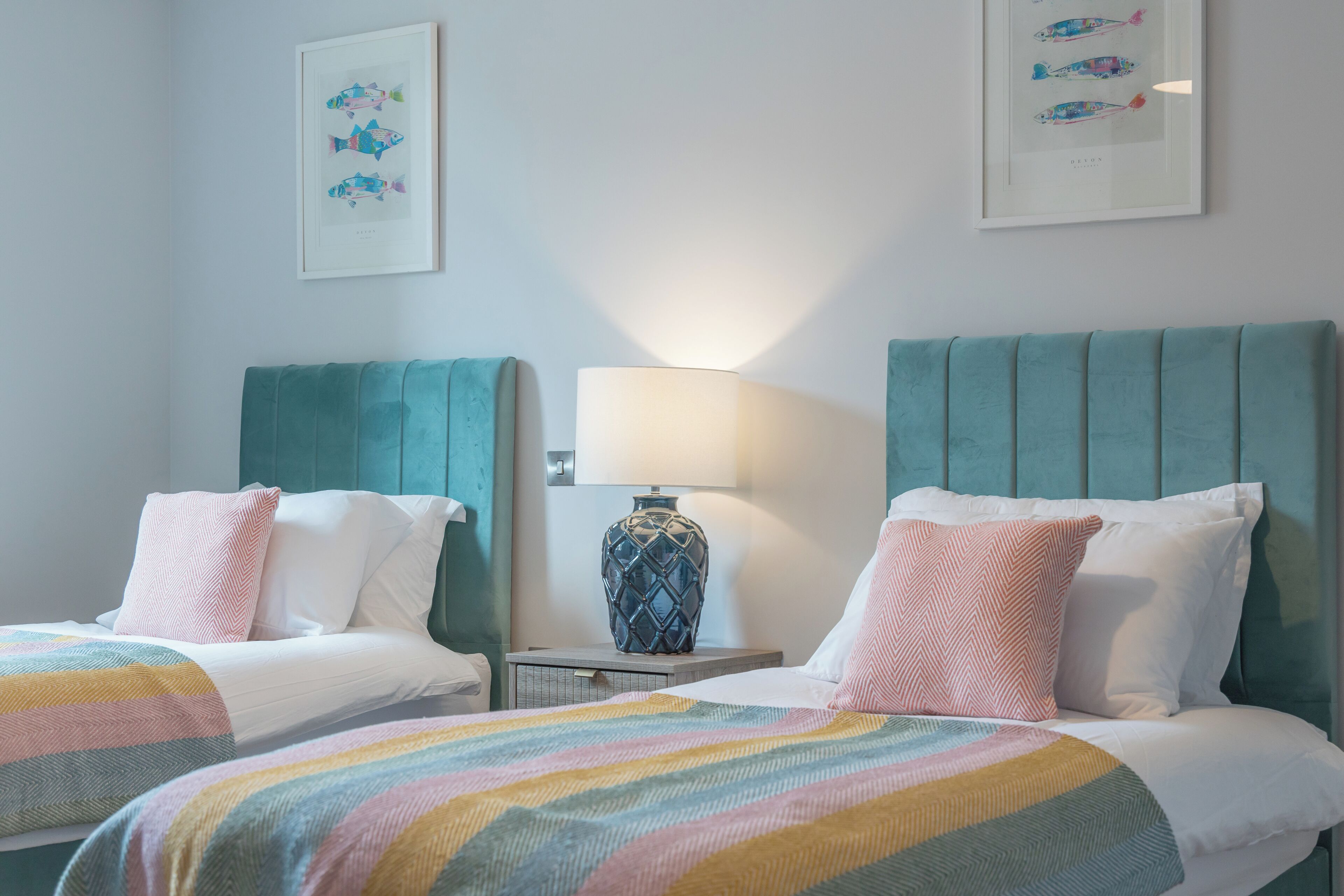 A hotel room with two beds, a nightstand with a lamp, and framed artwork on the wall.