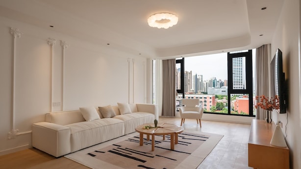 Een moderne woonkamer met een bank, een ronde salontafel en een stadsgezicht door grote ramen.