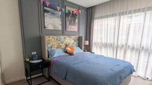 Een slaapkamer met een bed, nachtkastje, lamp en een raam met gordijnen.