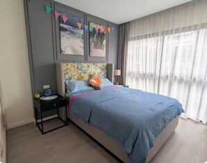 Un dormitorio con una cama, una mesita de noche, una lámpara y una ventana con cortinas.