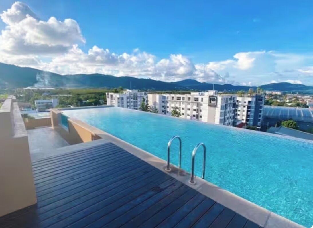 A swimming pool with a wooden deck, surrounded by buildings and mountains.