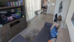 Een woonkamer met een televisie, bank en een eethoek met een tafel en stoelen.