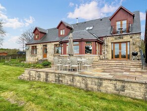 A stone house with a patio, outdoor seating, and a barbecue.