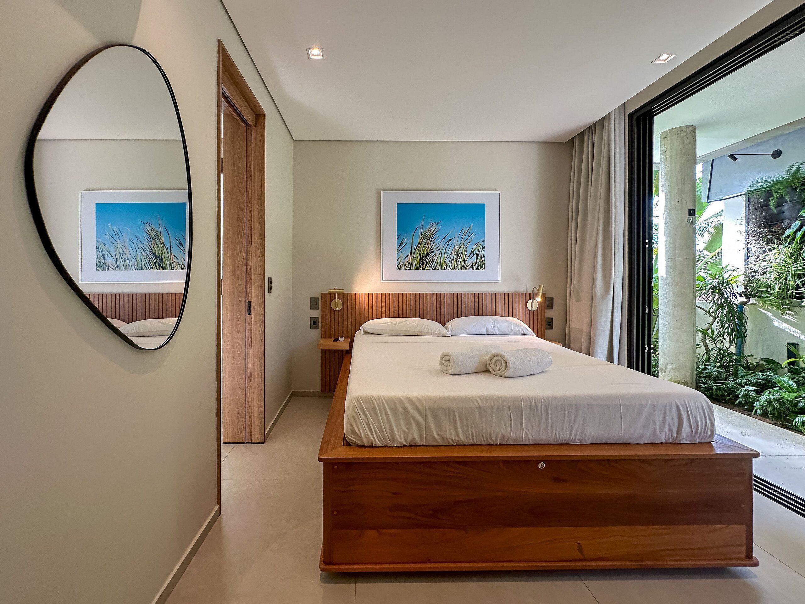 Un dormitorio moderno con una cama grande, cabecera de madera, una mesita de noche, un espejo y dos cuadros enmarcados en la pared.