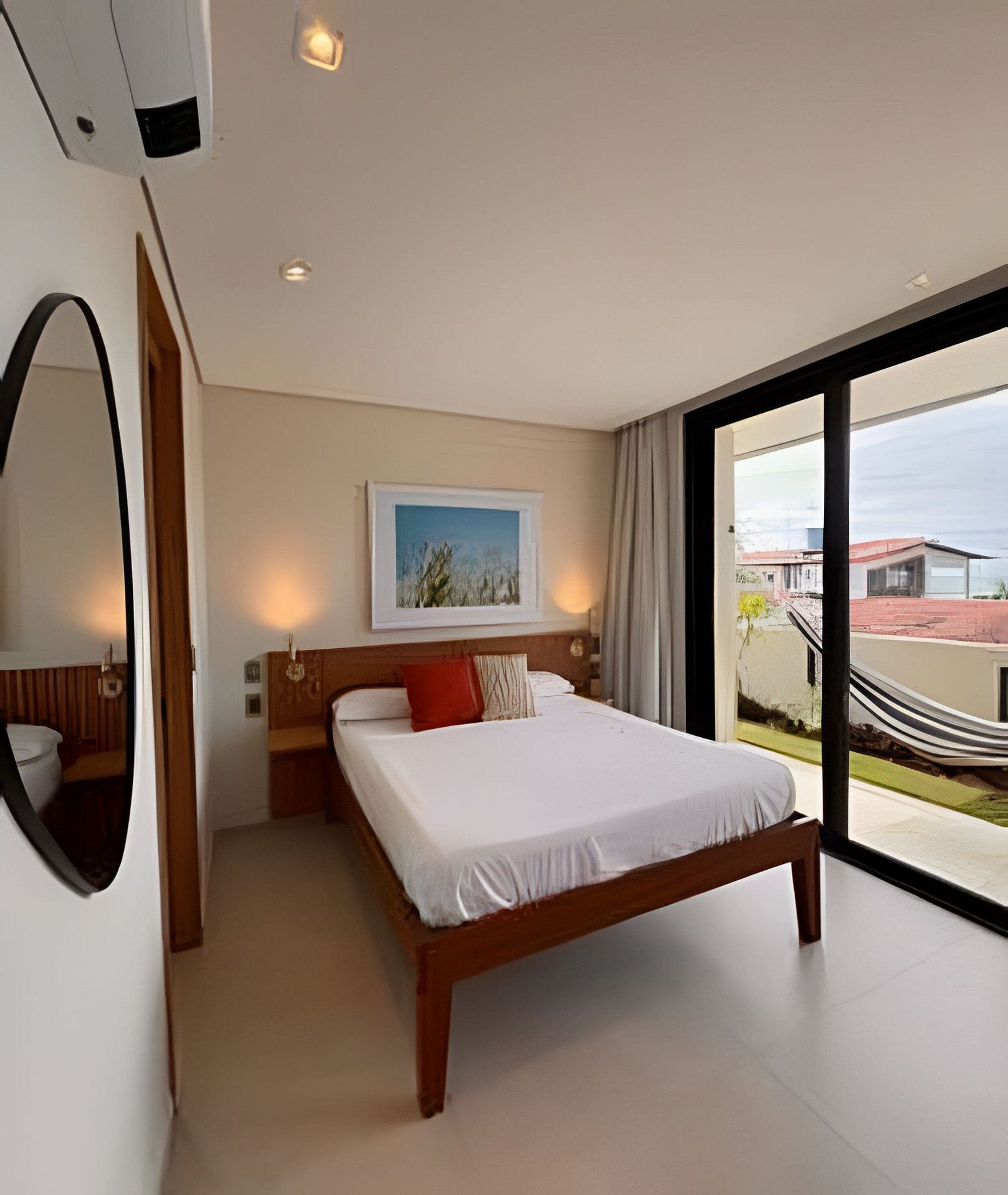 Una habitación de hotel moderna con una cama grande, un cuadro enmarcado en la pared y vistas de la ciudad a través de la ventana.