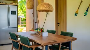 A modern kitchen with a wooden dining table, green chairs, and hanging woven light fixtures. - Vila Manga Rosa (Tibau do Sul)
