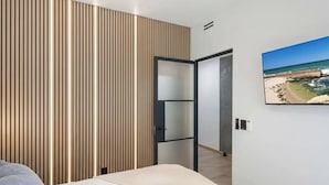 A modern bedroom with a bed, a wooden slat wall, a TV, and a beach view. - Walk to Gaslamp & Petco • Rooftop Spa & Game Room (San Diego)