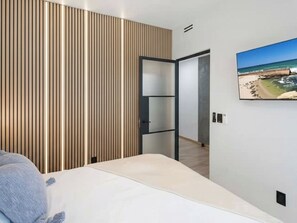 Un dormitorio moderno con una cama, un panel de madera, un televisor y vista al mar.