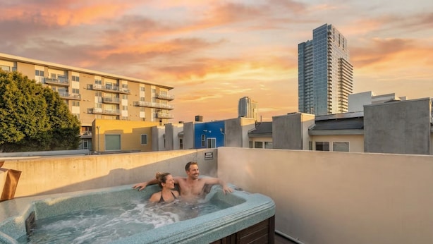 A couple relaxing in a hot tub on a rooftop with a cityscape view. - Walk to Gaslamp & Petco • Rooftop Spa & Game Room (San Diego)