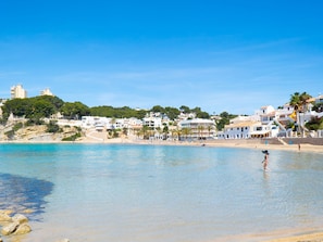Eine Küstenstadt mit Häusern entlang des Strandes, klarem blauen Wasser und einer Person, die im Wasser steht.