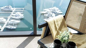 Ein Balkon mit Blick auf eine Marina, ein Stuhl mit einer Pflanze und zwei schwarze Tassen auf einem Tablett.