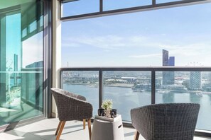 A balcony with wicker chairs, a small table, and a view of a cityscape and water. - Harbour View 2BR Docklands Apt Near Marvel Stadium (Docklands)