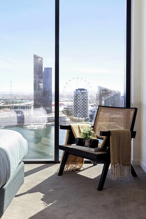A modern room with a large window, a bed, a chair with a plant, and a view of a cityscape. - Harbour View 2BR Docklands Apt Near Marvel Stadium (Docklands)