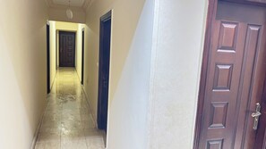 Un couloir avec un sol carrelé, une porte en bois sur la droite et une porte au fond.