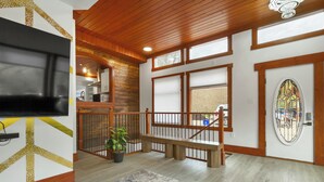 A spacious interior with a wooden staircase, a flat-screen TV, a potted plant, and a decorative door. - Spacious Modern Entire Main House & Suite - Sleeps 16 (Vernon)