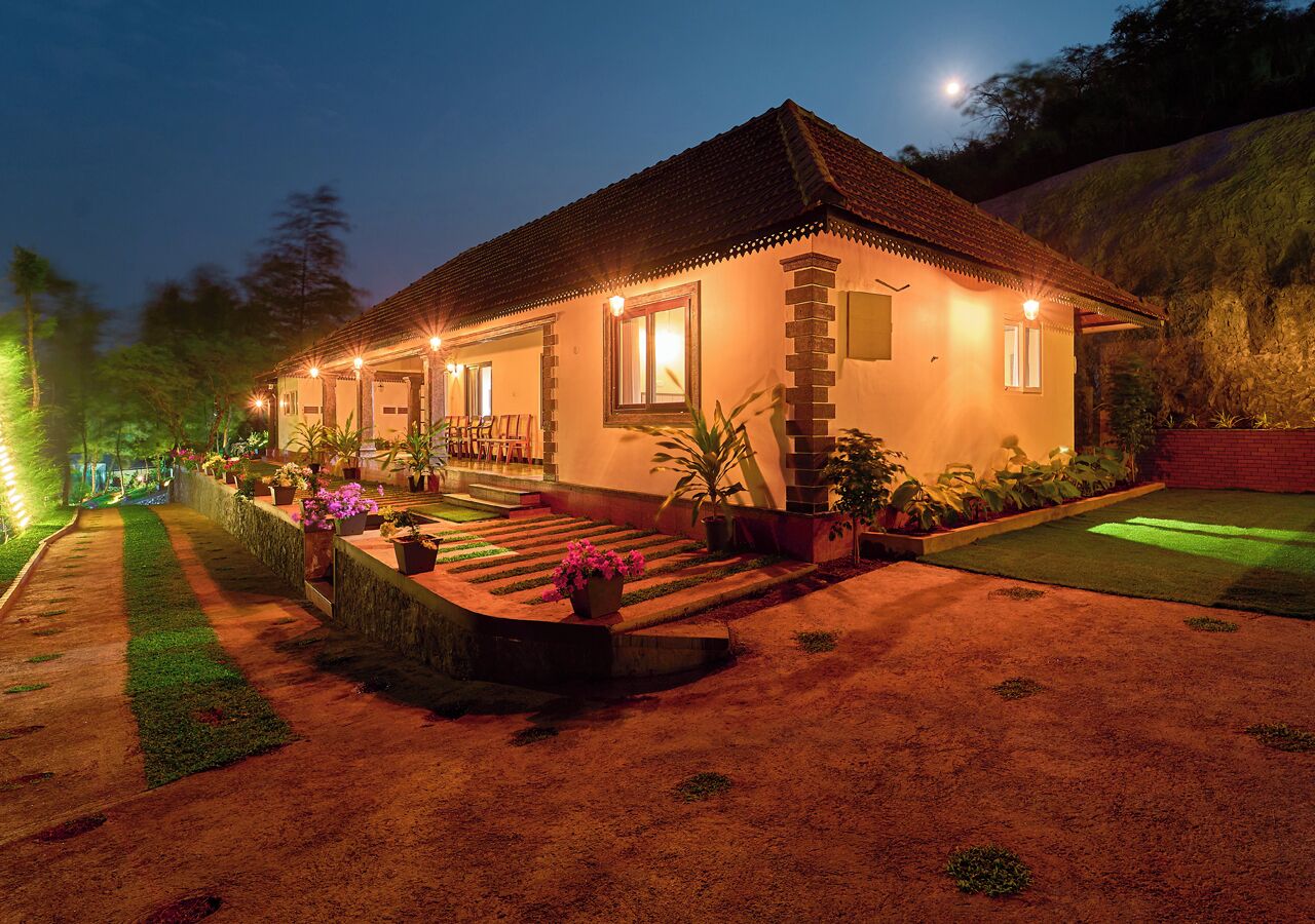 A two-story house with a tiled roof, a front porch with chairs, and a well-lit entrance.
