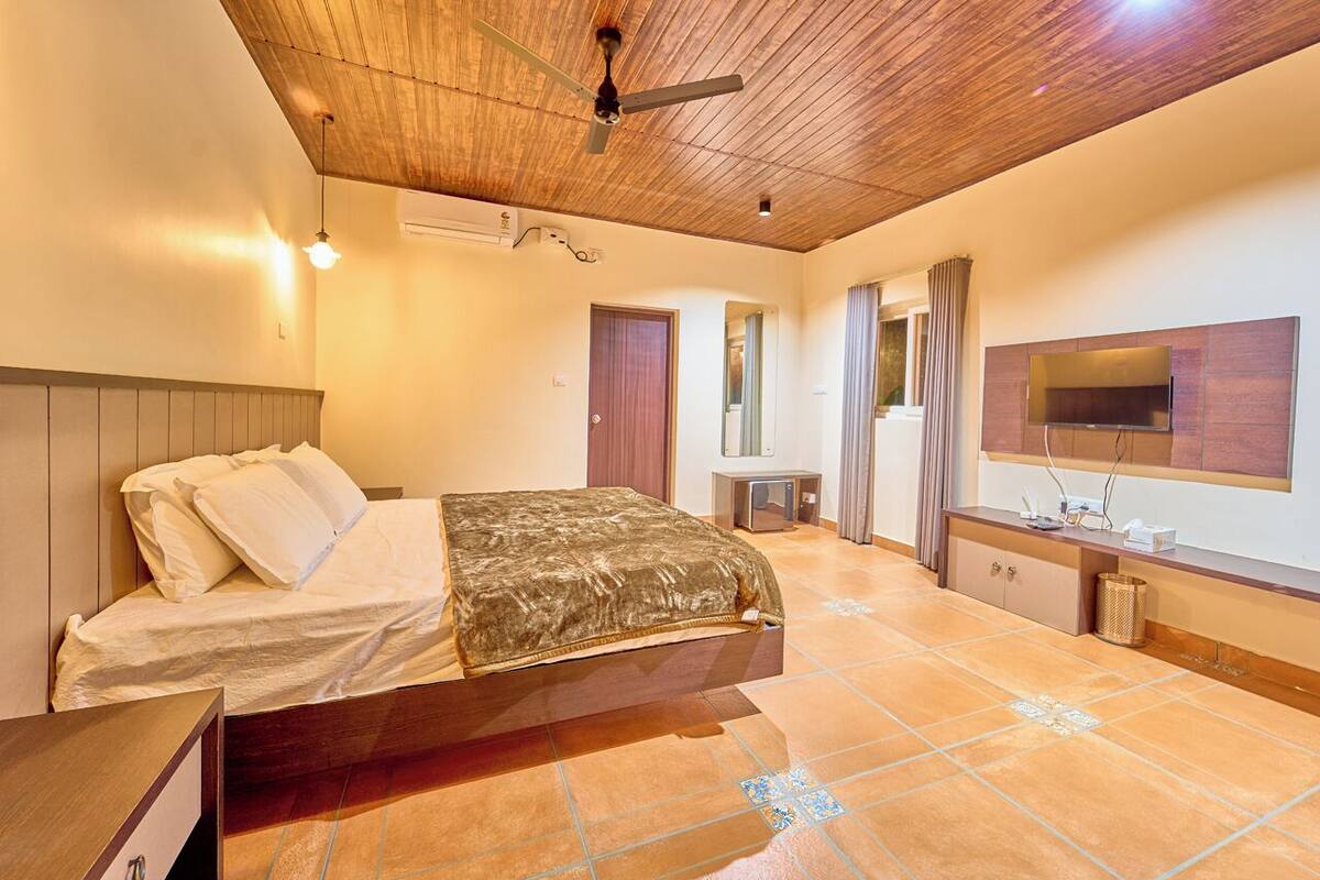 Quarto com cama, TV, ventoinha no teto e piso ladrilhado.