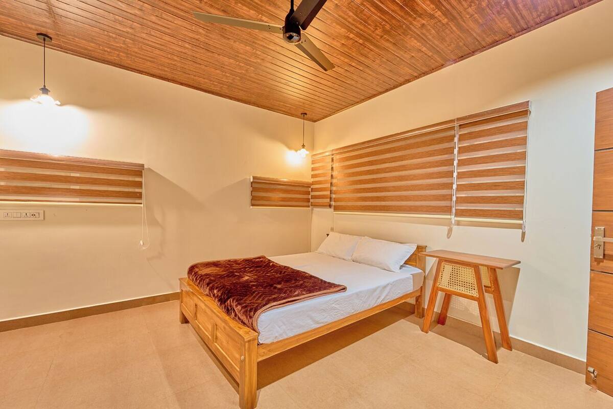 Quarto com uma cama de madeira, uma pequena mesa de madeira e um ventilador de teto.